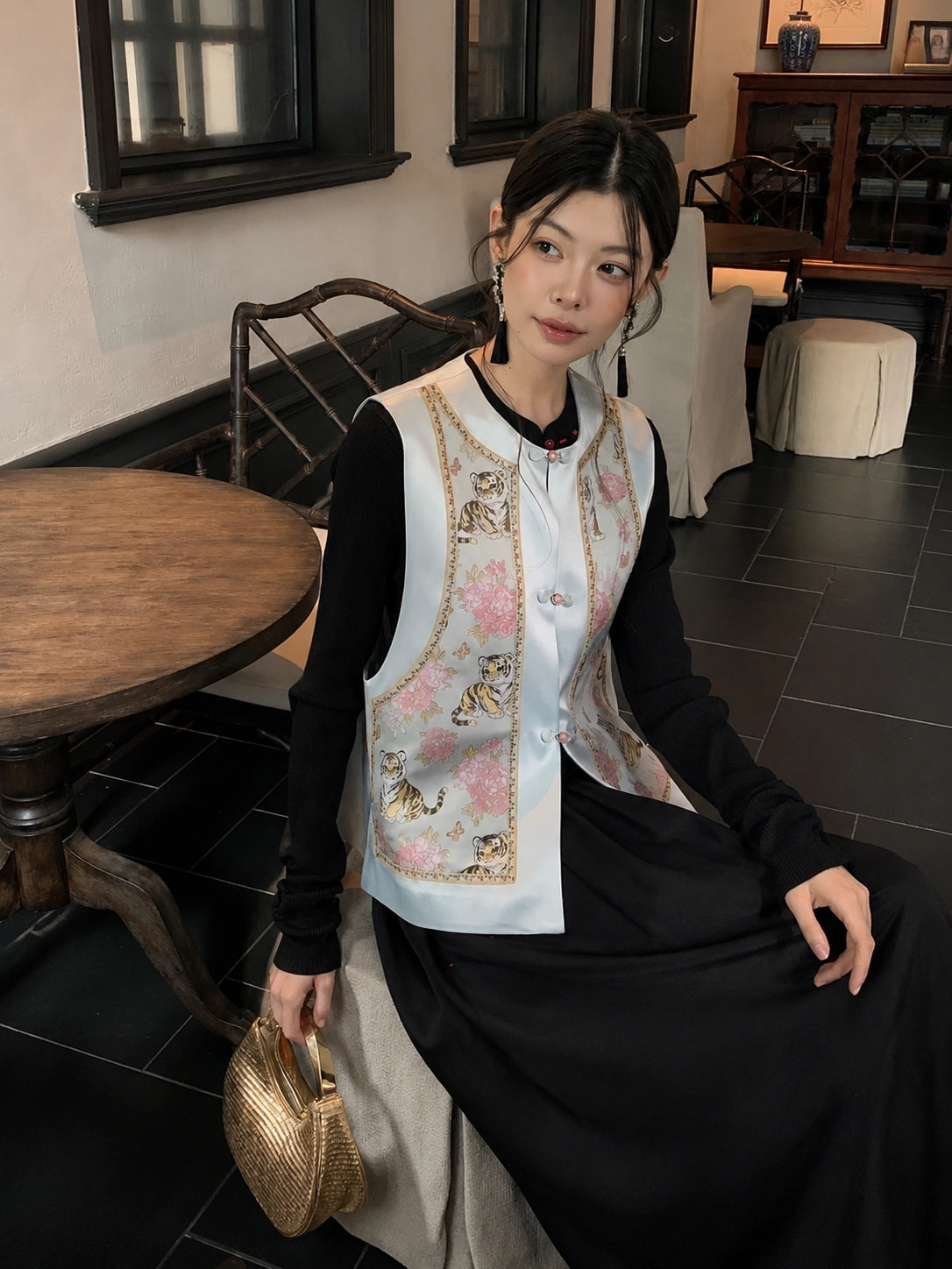Seated styling image of a light blue Chinese-style silk vest with botanical floral pattern, paired with a black skirt.