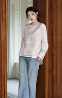 Model leaning by a doorway in the pink jacquard vest and white inner top.
