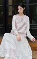 Seated model wearing the pink vest and white inner top with a textured white skirt.