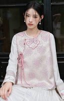 Seated model wearing the pink vest over a white inner top beside a dark window.
