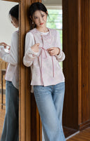 Model holding the pink side tie of the jacquard vest while wearing it with a white top and jeans.
