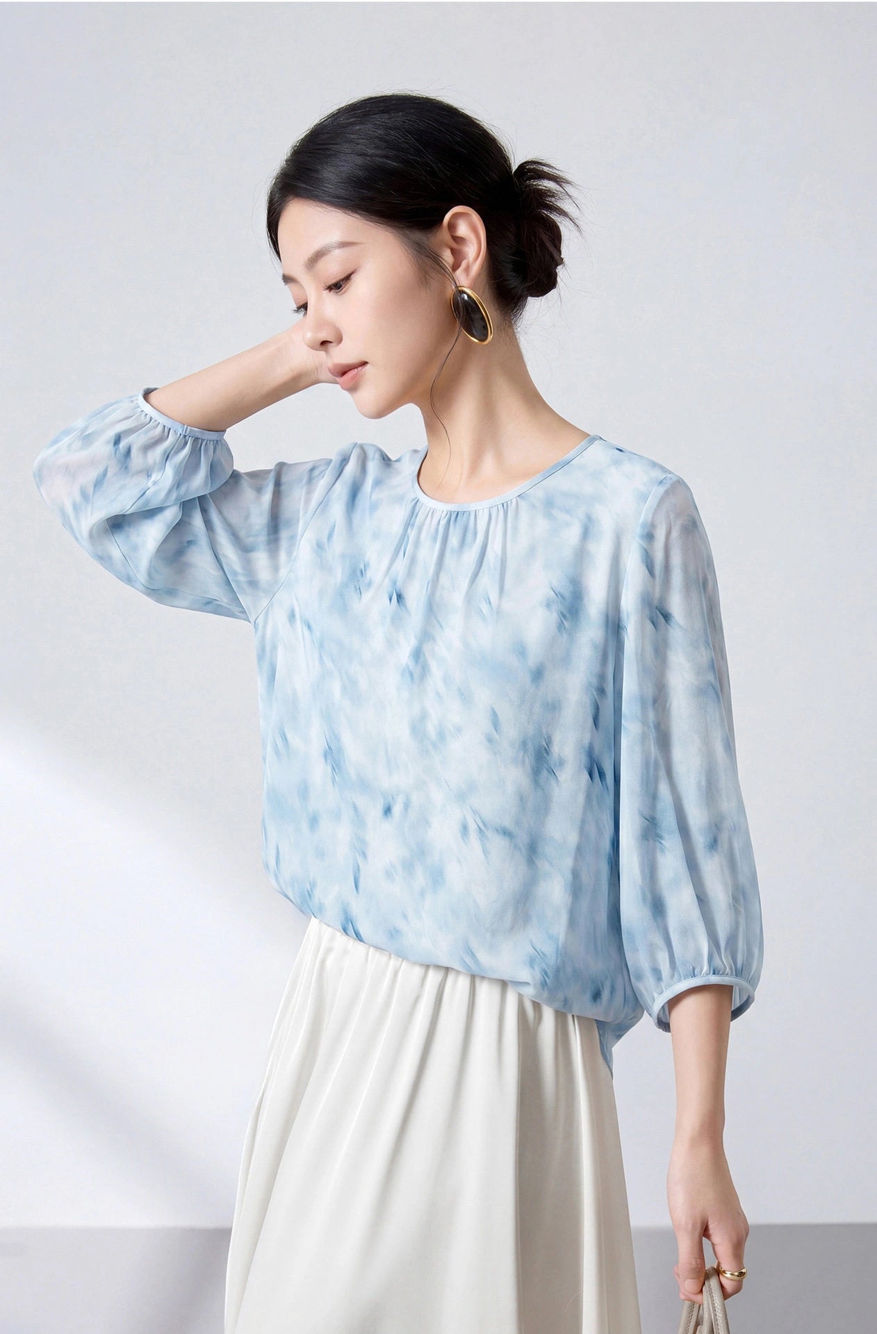 Three-quarter view of a lightweight sky blue silk blouse with gathered cuffs and an abstract print