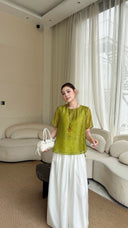 Front view of a lime green short sleeve top with a round neck, paired with white wide-leg pants and a white handbag.
