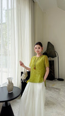 Model wearing a bright green short sleeve blouse with a relaxed fit, styled with white trousers and a white bag.