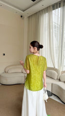 Back view of a lime green short sleeve top with a tie closure at the back of the neck, paired with white wide-leg pants.