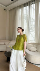 Side view of a woman wearing a bright green blouse with short sleeves and a round neck, holding a white handbag, showcasing the elegant drape.