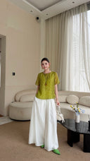 Full body shot of a green short sleeve shirt with a relaxed silhouette, paired with white wide-leg pants and a white handbag.