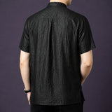 Back view of the black silk shirt, highlighting the natural drape and a central pleat detail at the back yoke.