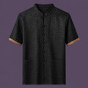 Flat lay of the men's short-sleeve silk top, featuring a stand collar, six front frog buttons, two patch pockets, and distinctive brown cuffs.