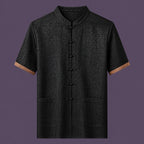 Flat lay of the men's short-sleeve silk top, featuring a stand collar, six front frog buttons, two patch pockets, and distinctive brown cuffs.