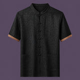 Flat lay of the men's short-sleeve silk top, featuring a stand collar, six front frog buttons, two patch pockets, and distinctive brown cuffs.
