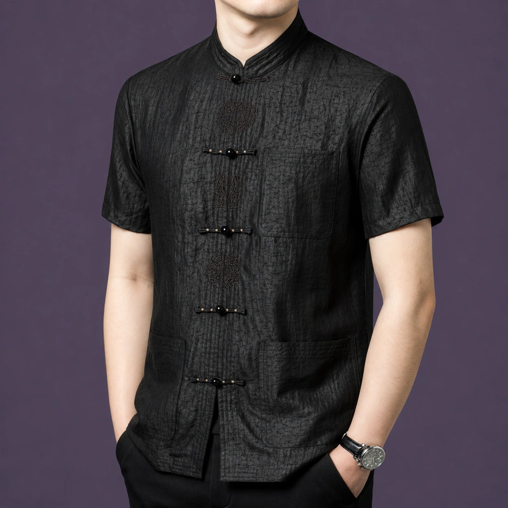 Front view of the black silk top showcasing the intricate embroidery detailing on the frog button placket and three patch pockets.