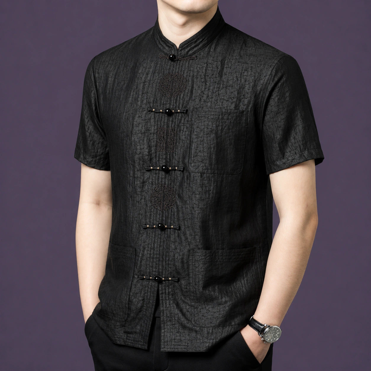 Front view of the black silk top showcasing the intricate embroidery detailing on the frog button placket and three patch pockets.