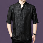 Men's black textured silk top with a simple stand collar and V-neckline, styled with black trousers and a watch.