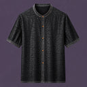 Flat lay of a black men's short-sleeve silk shirt with a mandarin collar, contrasting amber buttons, and a distinctive textured finish.