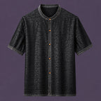 Flat lay of a black men's short-sleeve silk shirt with a mandarin collar, contrasting amber buttons, and a distinctive textured finish.