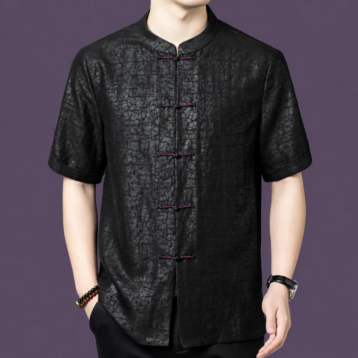 Men's black silk top with frog-button placket, styled with a watch and beaded bracelet, highlighting the versatile casual look.
