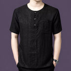 Men's black 100% mulberry silk short-sleeve henley shirt with a round neck, 3-button placket, and single chest pocket, styled with black trousers.