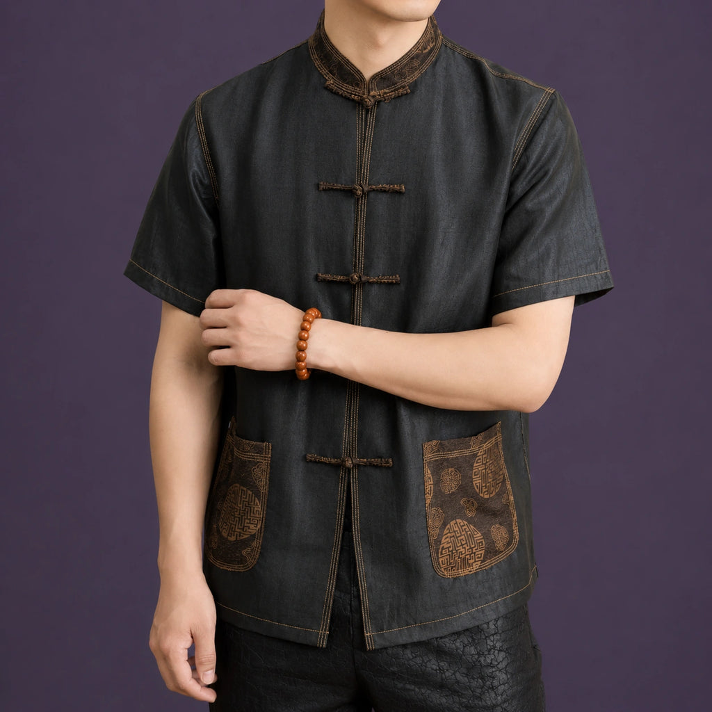 Close-up of the Mandarin collar, frog buttons and embroidered pockets on a men's black mulberry silk Tang shirt.