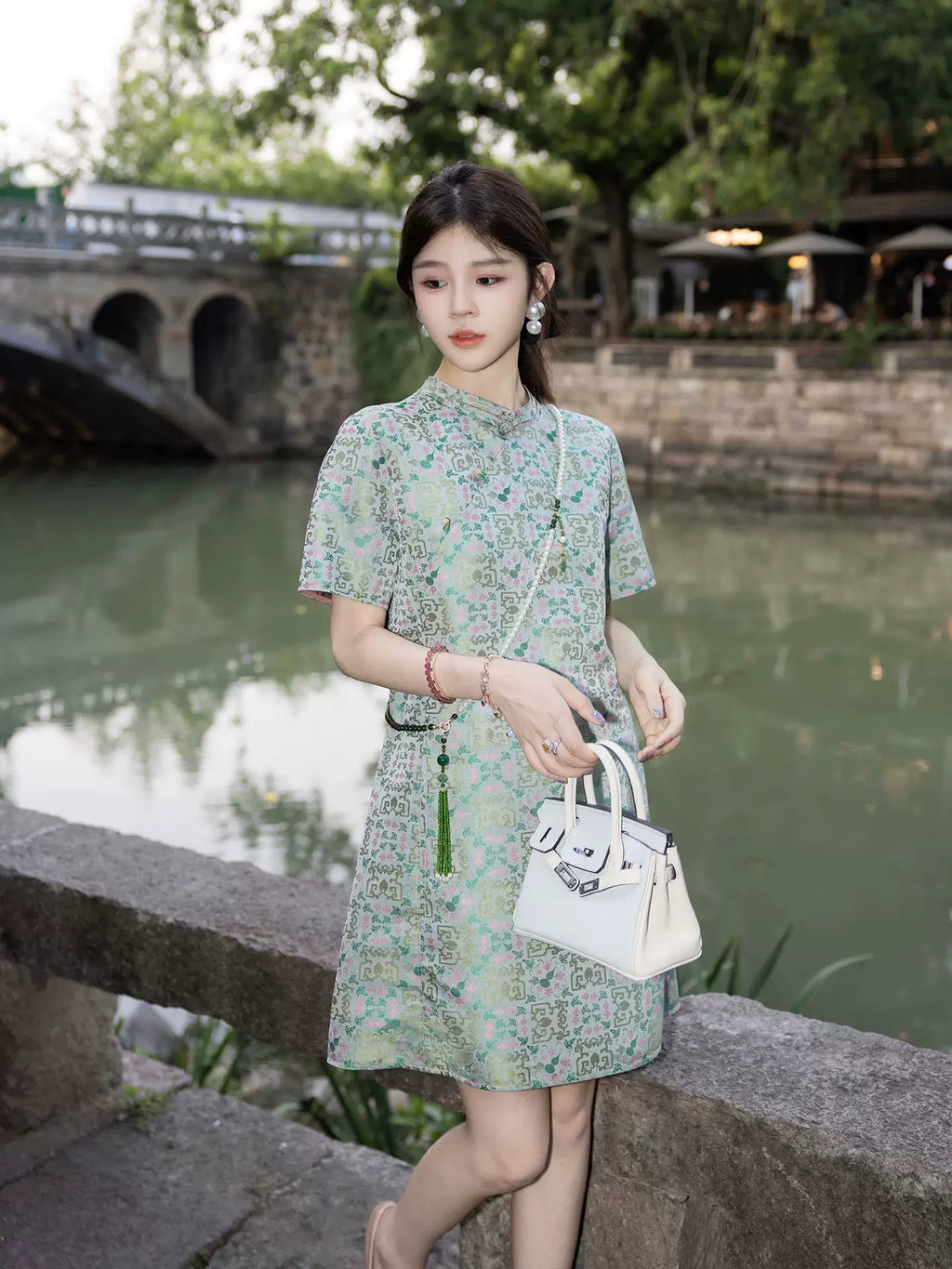 Model wearing a mint green printed silk-blend dress beside a traditional Chinese canal