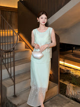 Model wearing a mint green sleeveless top and matching skirt with beaded neckline, standing on stairs, holding a white handbag.