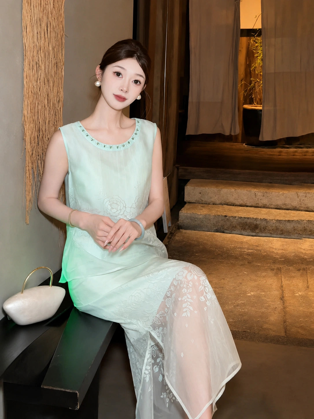 Sitting model in a mint green sleeveless top and midi skirt with a sheer white hem, holding a white bag, highlighting the comfortable fit and relaxed silhouette.