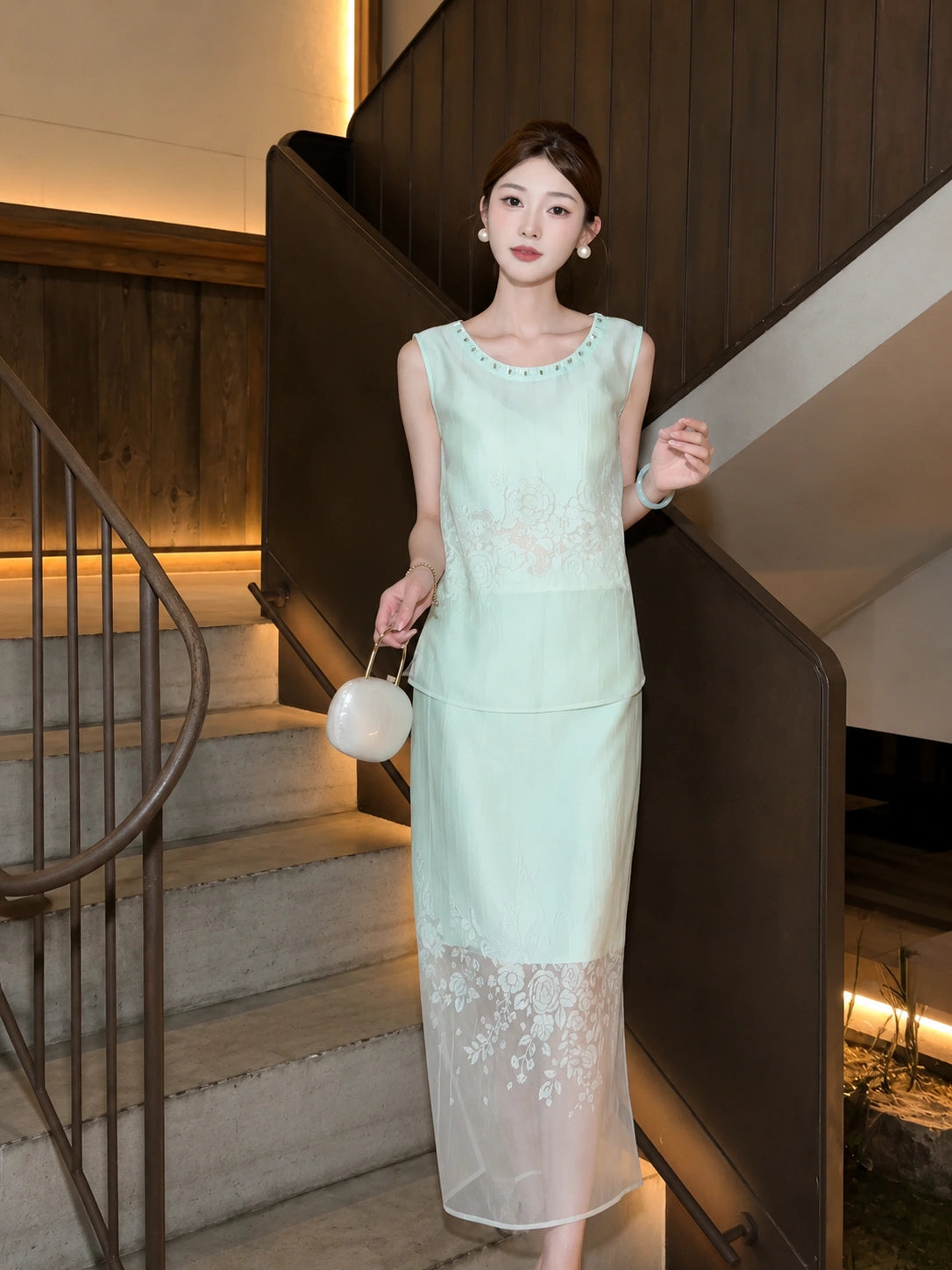 Model on stairs in a mint green sleeveless top and skirt set with a white layered hem and beaded neckline, showcasing the full outfit.