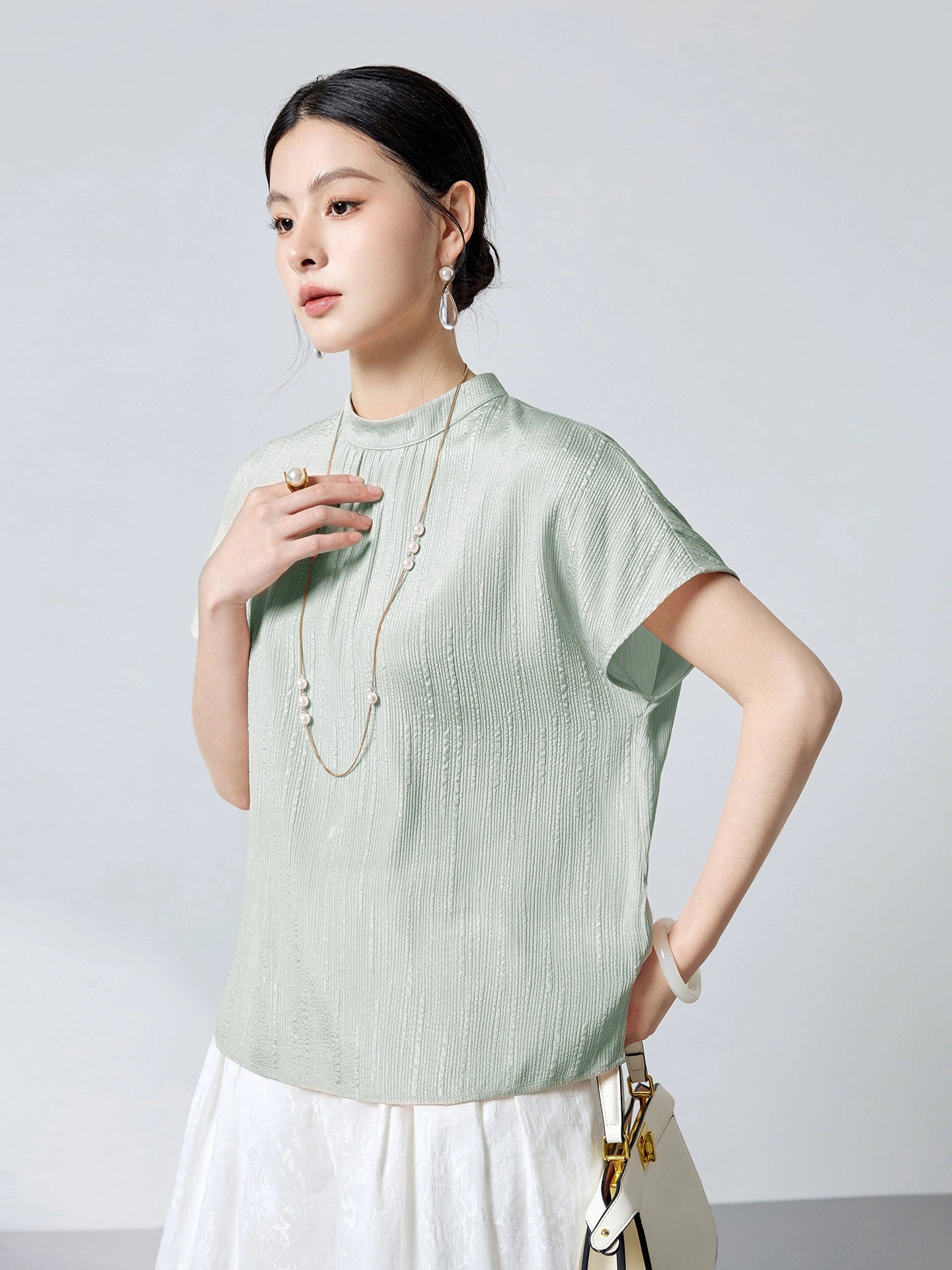 Model wearing a mint green silk top with a stand collar and short sleeves, showcasing the lightweight and breathable 91.1% Mulberry Silk blend.
