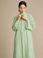 Front view of the model buttoning up the mint green long dress, emphasizing the natural "paper-like" crinkled texture of the lyocell-linen blend.