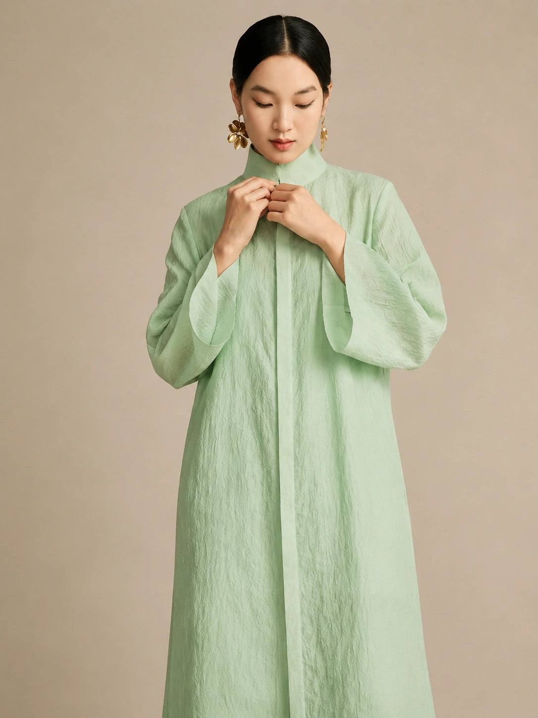 Front view of the model buttoning up the mint green long dress, emphasizing the natural "paper-like" crinkled texture of the lyocell-linen blend.