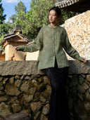 Model extending both arms to show the generous sleeves, relaxed shape and side slits of a muted green shirt.