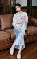 Model seated in the mist silver vest layered over a white top and pale blue skirt.