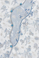 Close-up of the curved front placket with blue buttons, piping and floral embroidery.