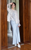 Full-length doorway view of the jacquard vest styled with a white inner top and pale blue skirt.