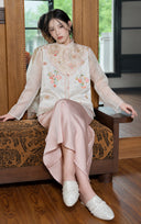 Front view of a seated model wearing the porcelain white embroidered vest over a sheer blouse.