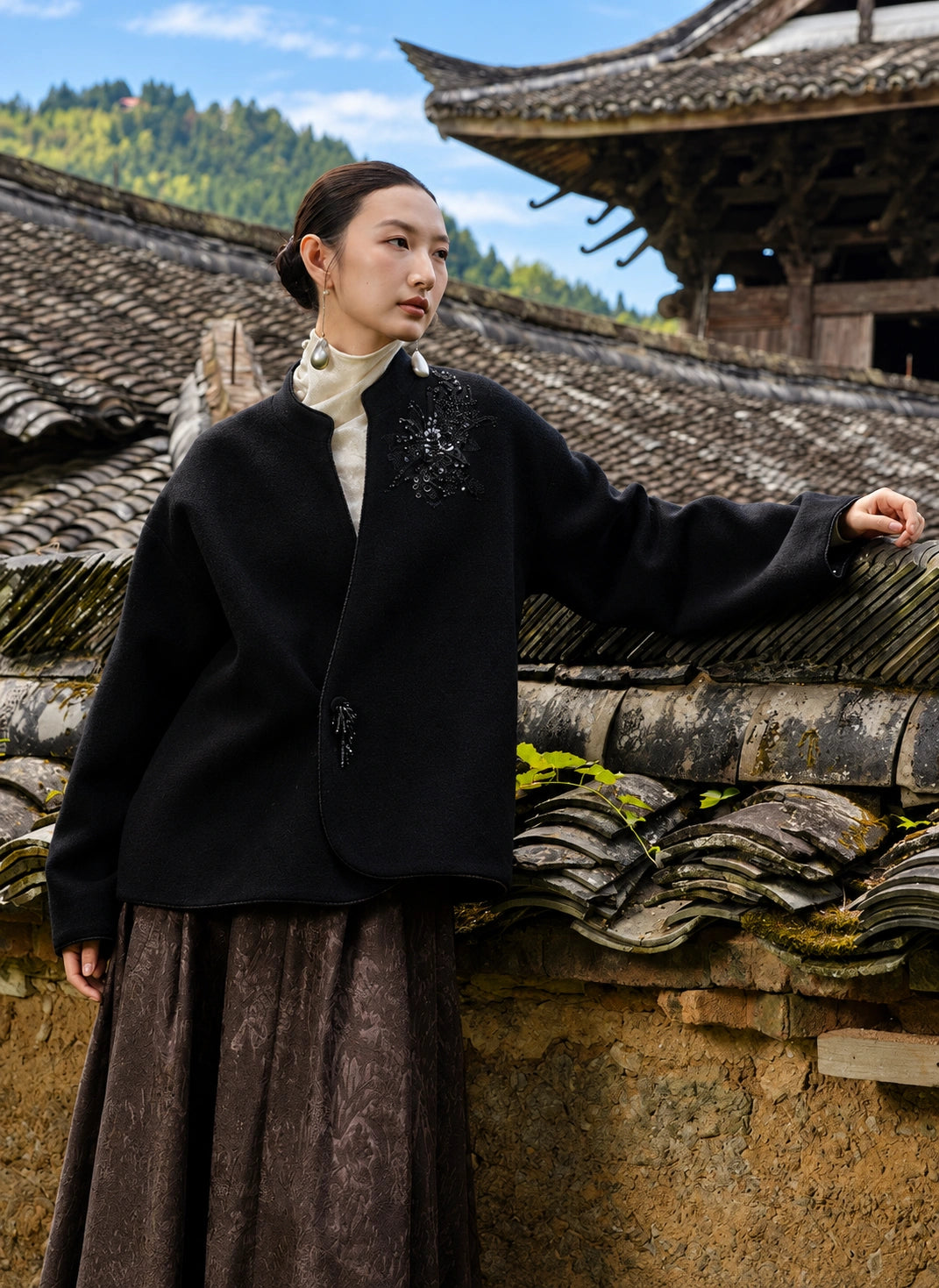 Model wearing the Jinyu Black coat with one arm resting on a tiled wall.