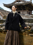Model wearing the black wool coat and brown skirt beside a tiled wall.