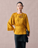 Woman wearing a mustard gold jacquard blouse with floral sequin embroidery