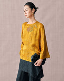 Three-quarter view of the mustard gold floral jacquard blouse styled with black separates