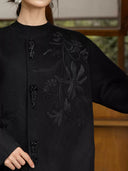 Close-up of black botanical embroidery, bead detailing and tassel fastenings on the Nanqiao coat.