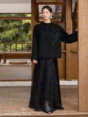 Full-length outfit featuring the Nanqiao black wool coat with a long textured black skirt beside a wooden pillar.
