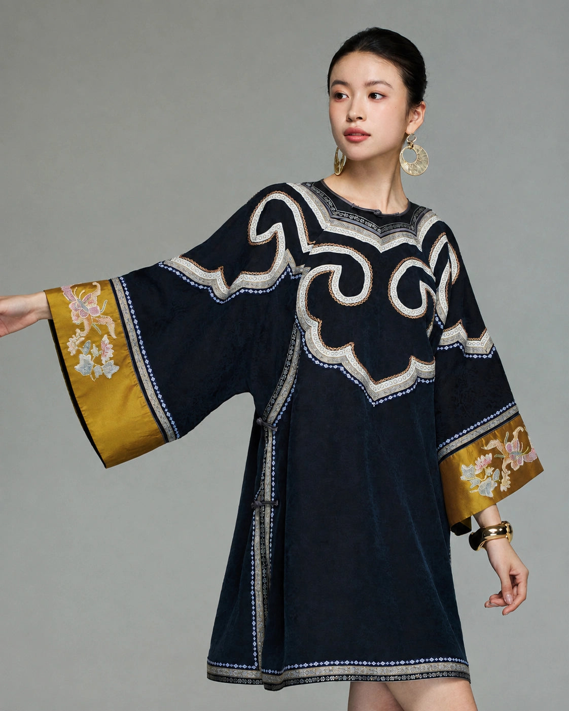 Close styling view of the embroidered scroll design and antique-gold floral cuffs on the navy silk dress