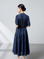 Back view of a navy blue silk jacquard dress with a tie waist and gathered tiers, showcasing the beautiful drape and subtle sheen of the premium silk.