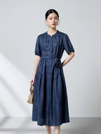 Front view of a navy blue 100% mulberry silk dress featuring a round neckline, puff sleeves, and a tie waist, showcasing the intricate dark pattern jacquard texture.