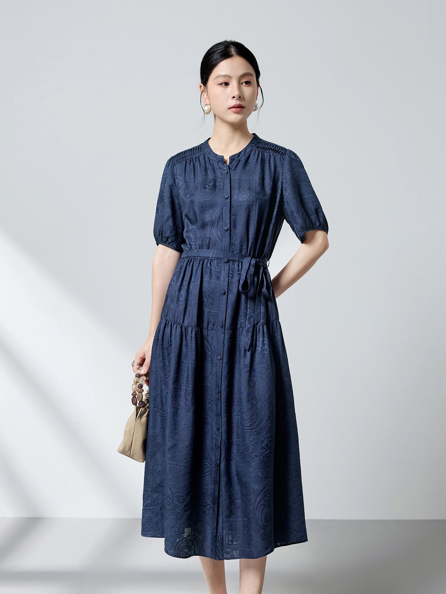 Front view of a navy blue 100% mulberry silk dress featuring a round neckline, puff sleeves, and a tie waist, showcasing the intricate dark pattern jacquard texture.