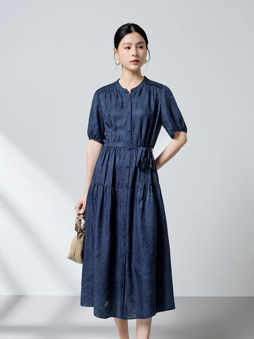 Front view of a navy blue 100% mulberry silk dress featuring a round neckline, puff sleeves, and a tie waist, showcasing the intricate dark pattern jacquard texture.