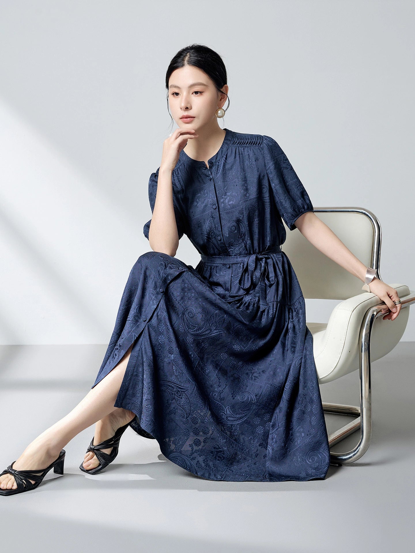 Sitting model in a navy blue silk dress with a tiered skirt and side slits, highlighting the elegant drape and flattering silhouette of the 100% mulberry silk fabric.