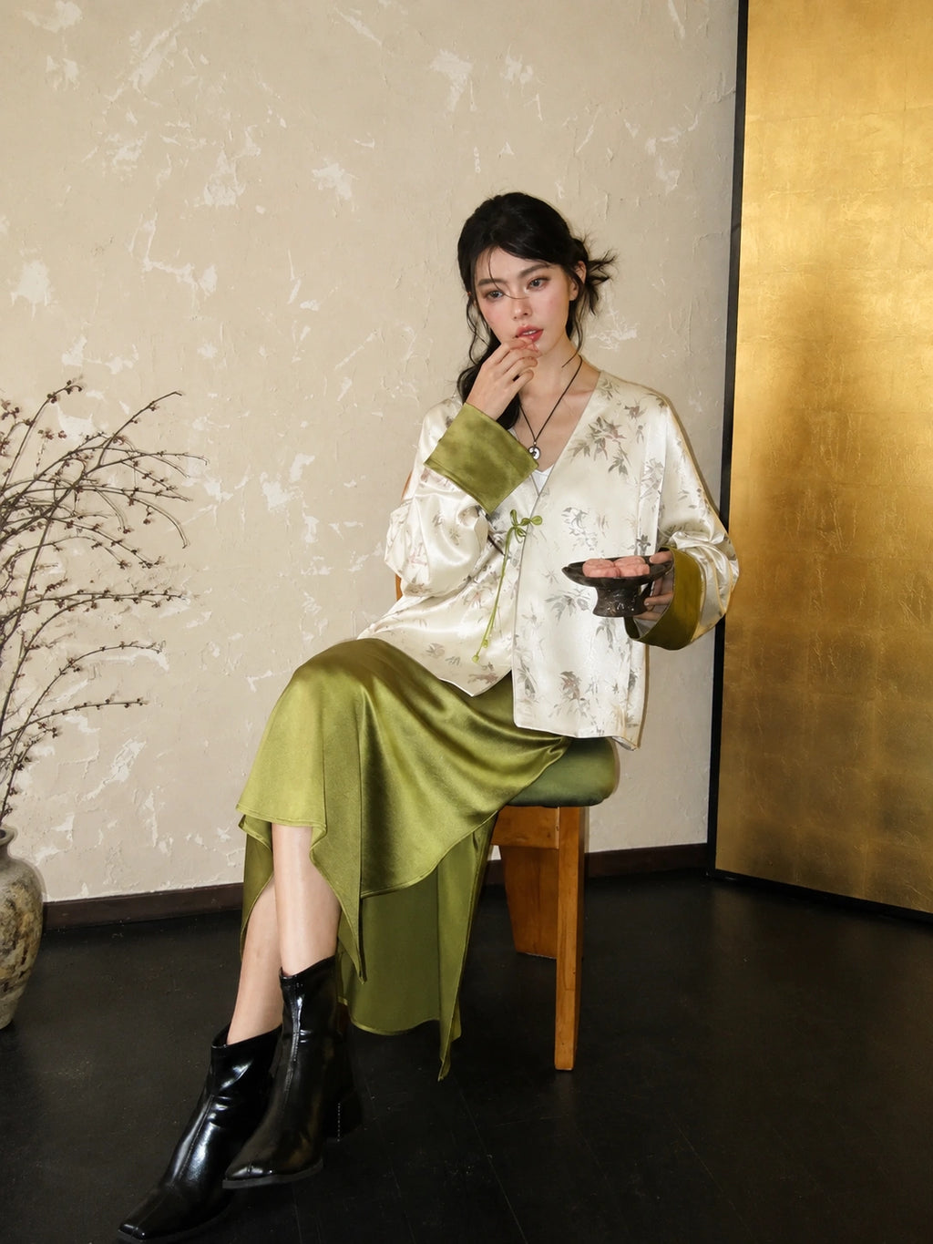 Seated styling image of a New Chinese-style white green acetate bamboo jacket paired with a glossy matcha green skirt.