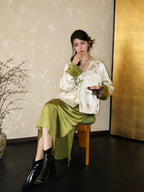 Seated styling image of a New Chinese-style white green acetate bamboo jacket paired with a glossy matcha green skirt.