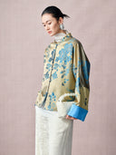 Woman wearing a gold and blue floral jacquard Mandarin collar jacket in a side view